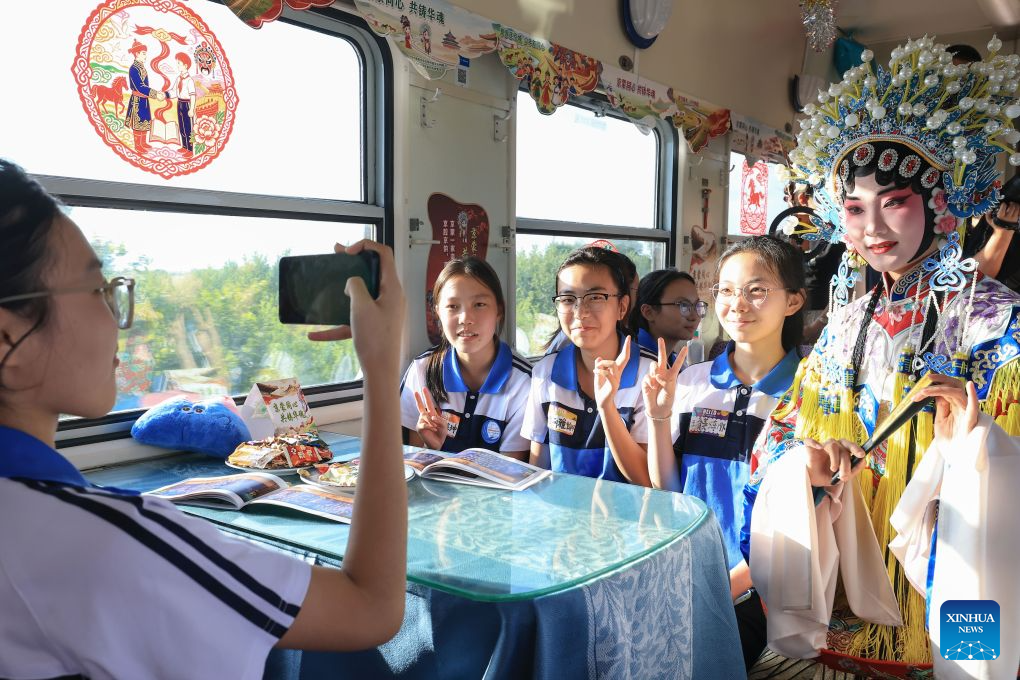 A Peking Opera actor poses for photos with students on a special train for study tour from northeast China's Heilongjiang Province to the capital city of Beijing on Aug. 9, 2026. The Y404 special train for a study tour carrying 598 teachers and students on Sunday departed from the Qiqihar railway station in northeast China's Heilongjiang Province to Beijing, capital of China.

The Heilongjiang-to-Beijing train is specially organized by China Railway Harbin Bureau Group Co., Ltd. this year for students on study tours, serving as a mobile classroom with singing and dancing activities held on it, where students on their way have the chance to interact and experience the charm of cultures. (Photo by Xu Shuai/Xinhua)