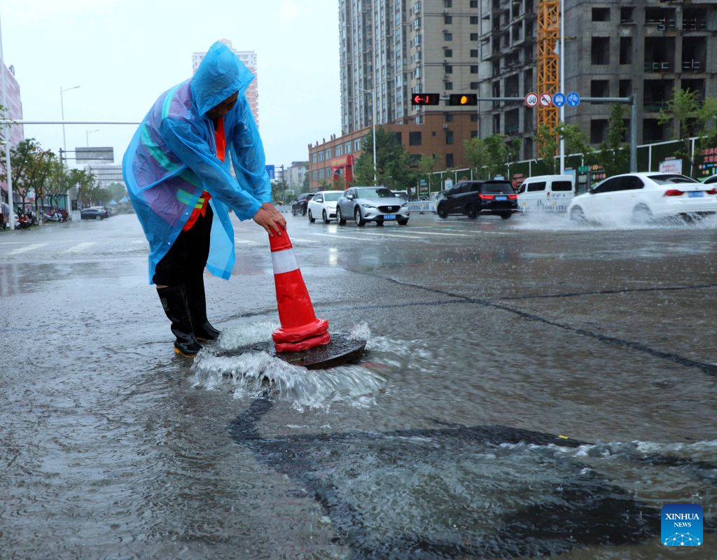 A sanitation worker places a traffic cone at a flooded spot of a road in Nanyang City, central China's Henan Province, Aug. 11, 2026. Torrential rains and flooding caused by Typhoon Dolphin, the 13th typhoon of the year, have swept vast regions in eastern and central China. Local authorities are exerting all efforts to eradicate potential risks and put people's life back to normal. (Photo by Gao Song/Xinhua)