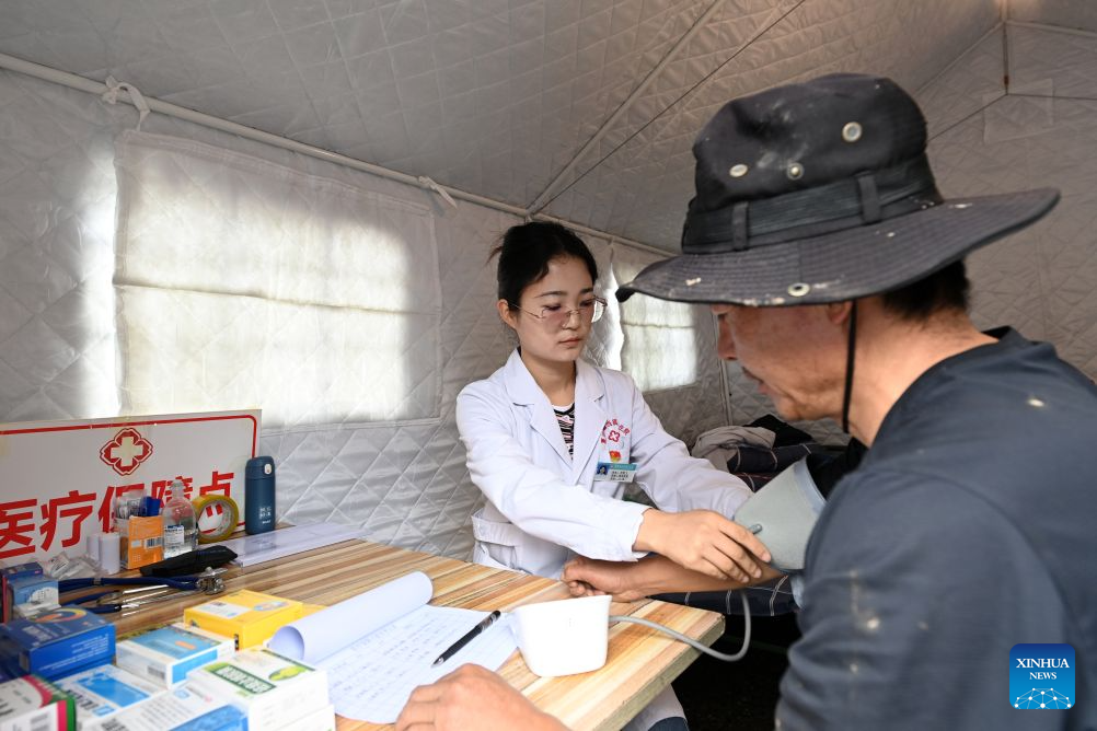 A medical worker measures blood pressure for a villager at a temporary relocation site in Madang Town, Xiahe County of the Tibetan Autonomous Prefecture of Gannan, northwest China's Gansu Province, July 16, 2026. Severe convective weather triggered mountain torrents here from July 13 to 14. Two temporary relocation sites were set up in Madang Town to accommodate 107 affected residents. (Xinhua/Fan Peishen)