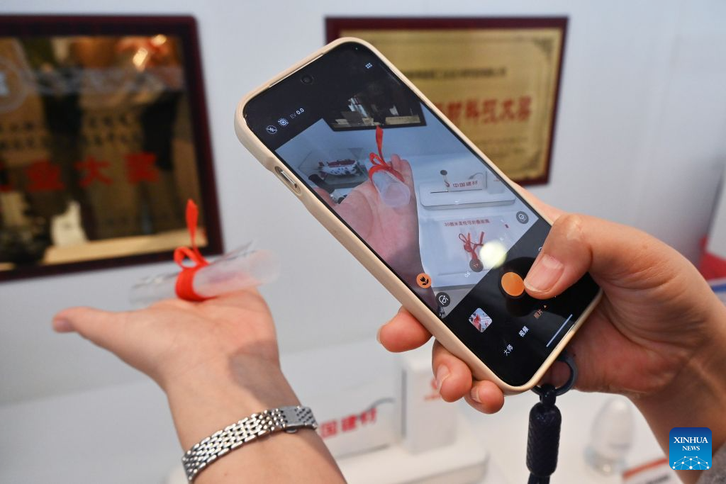 A visitor takes a photo of a foldable flexible glass sheet at the Bengbu Glass Industry Design and Research Institute of the China National Building Material Group Co., Ltd. in Bengbu, east China's Anhui Province, Aug. 8, 2026. Rooted in its glass industry, Bengbu has in recent years made breakthroughs in core technologies, successfully developed new glass products such as ultra-thin display glass and hollow glass microspheres, and established a complete industrial chain from quartz sand to end-user applications. (Photo by Lin Qiujin/Xinhua)