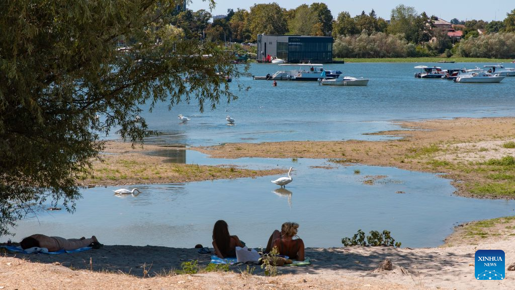 People rest on the bank of the Danube River in Belgrade, Serbia, on Aug. 16, 2026. Riverbed was exposed as the water level of the Danube River approached record-low by severe drought. (Photo by Wang Wei/Xinhua)