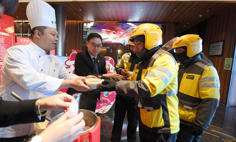 Food delivery riders sample porridge offered by a restaurant during a break between pickups in Beijing on January 26, 2026. Photo: VCG