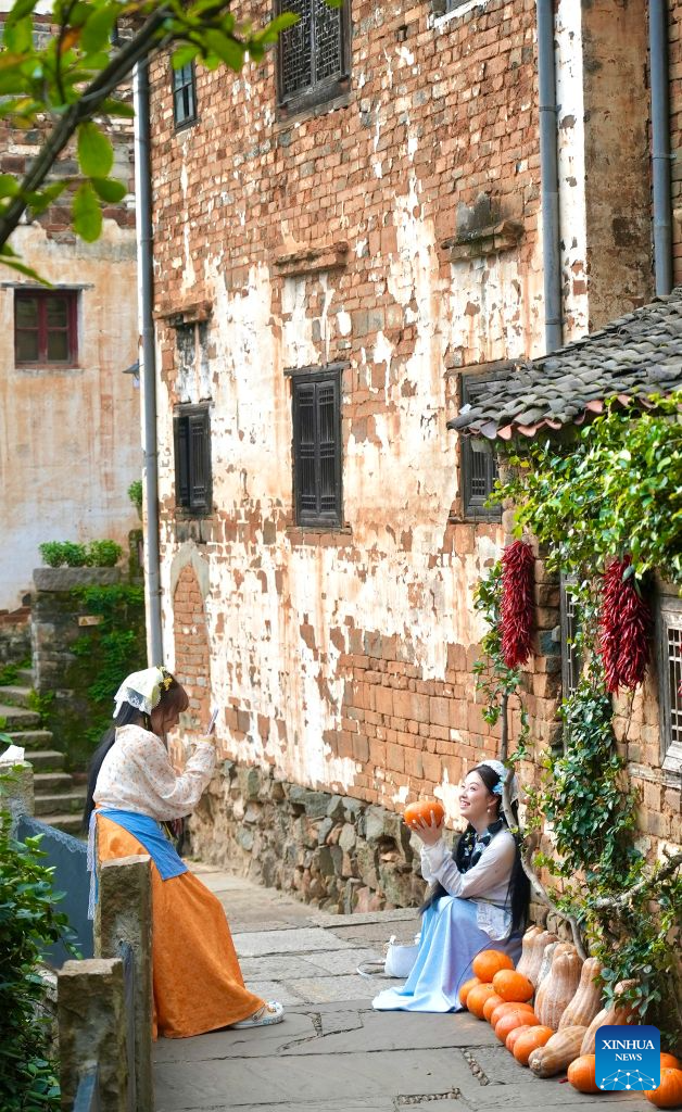 A tourist poses for a photo at Huangling Village in Wuyuan County, east China's Jiangxi Province, Aug. 25, 2026. As early autumn sets in, villagers in Huangling spread harvested crops on bamboo trays to dry. Colorful drying trays form a striking contrast against Hui-style houses with white walls and black tiles, drawing crowds of tourists. (Xinhua/Hu Chenhuan)