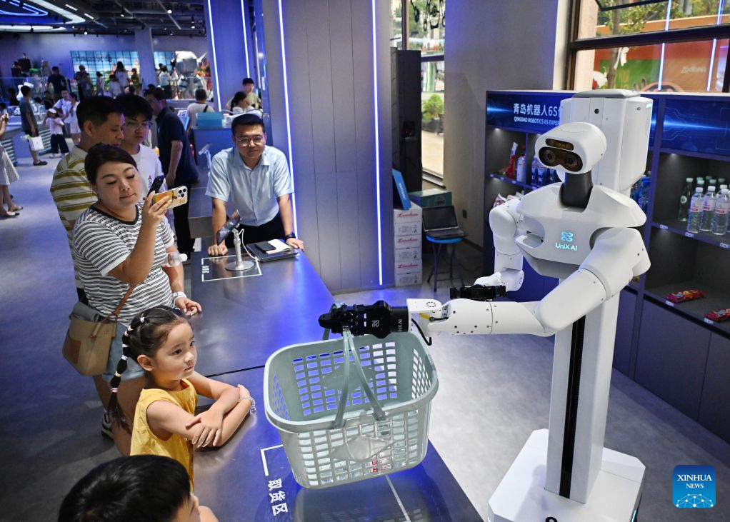 People interact with a robot at a robot 6S experience store in Qingdao, east China's Shandong Province on Aug. 11, 2026. Recently, the first robot 6S experience store in Qingdao opened, attracting a large number of consumers to visit and experience. This store integrates six major functions including sale, spare parts, service, survey, lease and personalized customization, helping further introducing robots into people's lives. (Xinhua/Li Ziheng)