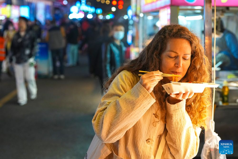 A Russian tourist tastes food at a night market in Heihe, northeast China's Heilongjiang Province, Sept. 15, 2026. Cross-border tourism and people-to-people exchanges between China and Russia have become more active since the introduction of optimized visa-free policies in 2025. (Xinhua/Na Yuqi)