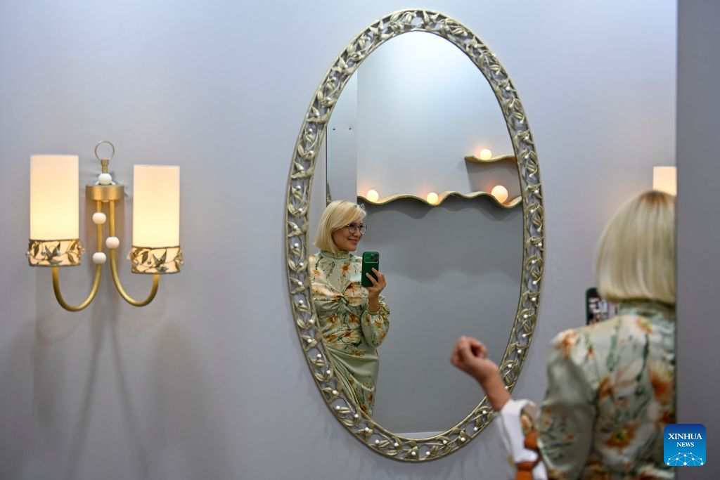 A woman takes photos of interior design works displayed at the Manege Central Exhibition Hall in Moscow, Russia, on Aug. 13, 2026. The 8th Moscow Interior and Design Week kicked off at the Manege Central Exhibition Hall here on Thursday. Under the theme Infinite Colours, the event draws participation from about 1,300 Russian and foreign brands and will run until Aug. 16. (Photo by Alexander Zemlianichenko Jr/Xinhua)