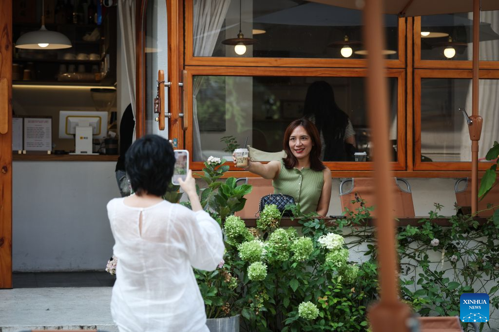 A tourist poses for a photo outside a coffee shop on Bajing Street, Shenyang City, northeast China's Liaoning Province, Aug. 1, 2026. A pack of coffee shops of varying styles on Bajing Street in Shenyang have breathed new life into the old city. Once quiet but obsolete, this historic street is now a vibrant new landmark of culture and tourism that attracts thousands of young visitors every day. Each coffee shop here tells a different story of how a city grows in time. (Xinhua/Pan Yulong)