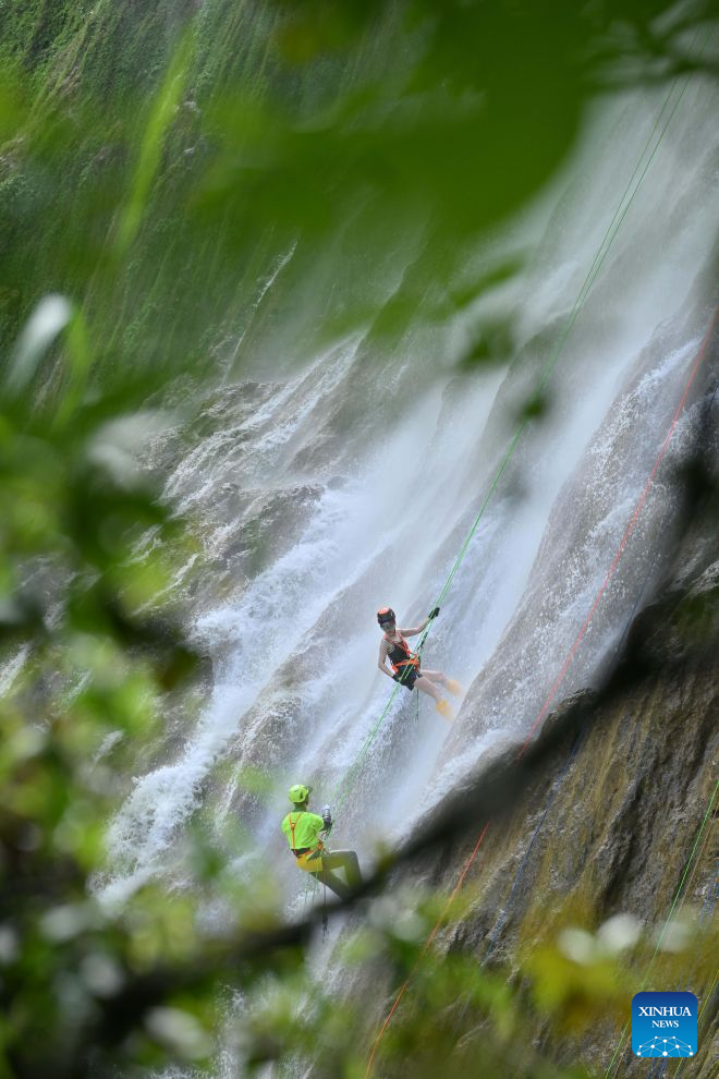 A tourist experiences waterfall rappelling under the guidance of a staff member at a scenic area in Huangping County, Qiandongnan Miao and Dong Autonomous Prefecture, southwest China's Guizhou Province, July 29, 2026. The waterfall rappelling here has attracted tourists for cool relief and exhilarating experience. (Photo by Zhang Ping/Xinhua)