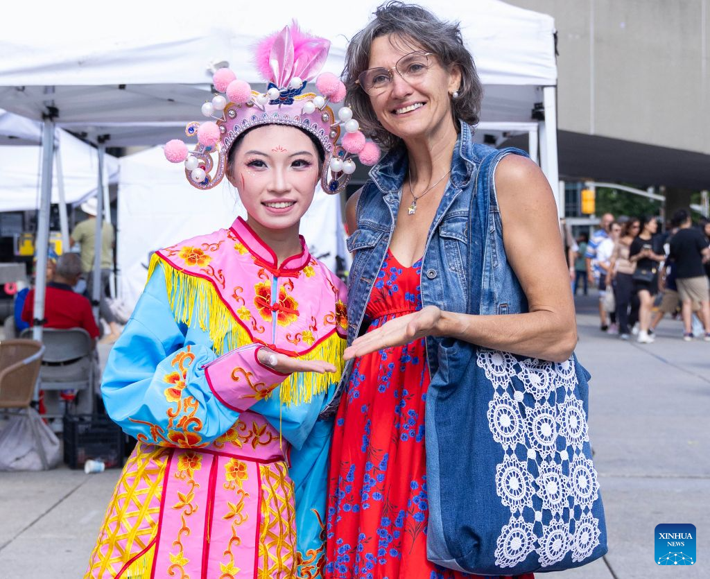 A woman poses for photos with a Yingge dance performer during the 2026 Toronto Dragon Festival at Nathan Phillips Square in Toronto, Canada, on Sept. 6, 2026. Hosted by the Canadian Association of Chinese Performing Arts (CACPA), this annual event was held here from Friday to Sunday to promote traditional Chinese culture through performing arts and related activities. (Photo by Zou Zheng/Xinhua)