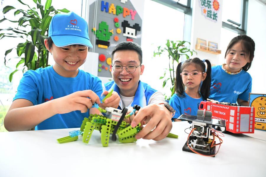 A volunteer (2nd L) instructs a child how to assemble a robot in Qingdao, east China's Shandong Province, July 24, 2026. (Xinhua/Li Ziheng)