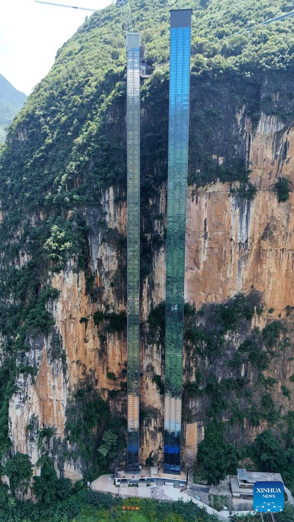 An aerial drone photo taken on July 31, 2026 shows two cliff elevators at Nizhu River Grand Canyon in Nizhuhe Village of Puli Township, Xuanwei City, southwest China's Yunnan Province. A 288-meter-high cliff elevator began operation recently at Nizhu River Grand Canyon, side by side to another one of its kind already in service since 2022. This is expected to further facilitate local students' trips to their schools.
Nizhuhe Village is a small hamlet nestled in a deep valley carved by the Nizhu River meandering from south to north. In the past, the shortest route from the valley floor to the mountaintop was a steep cliffside path, and the round trip took nearly six hours. Children and their parents had to make the arduous journey at least once every 10 days.
In 2022, a significant change came to this challenging journey. Nizhu River Grand Canyon scenic area was completed and opened, with a 268-meter-high cliff elevator and a cable car system put into operation. The facilities are open free of charge to local villagers.
Today, the combination of sightseeing shuttle vehicles, elevators and cable cars has shortened students' journey to school to about 30 minutes. A dedicated passage has also been set up for the students, with police officers and dedicated staff members as their guardians along the trips. (Xinhua)