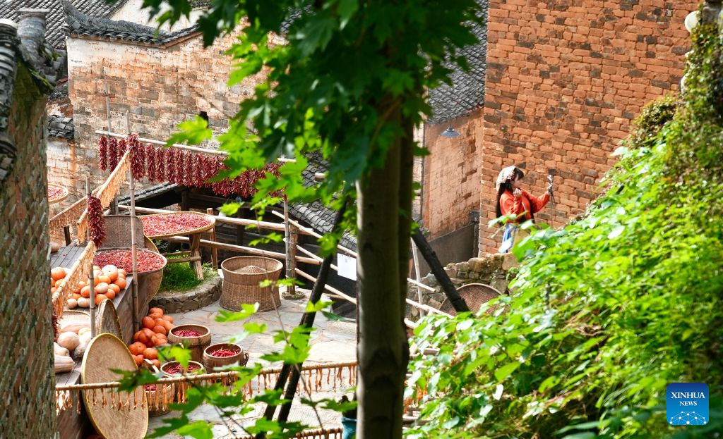 A tourist takes a selfie at Huangling Village in Wuyuan County, east China's Jiangxi Province, Aug. 25, 2026. As early autumn sets in, villagers in Huangling spread harvested crops on bamboo trays to dry. Colorful drying trays form a striking contrast against Hui-style houses with white walls and black tiles, drawing crowds of tourists. (Xinhua/Hu Chenhuan)