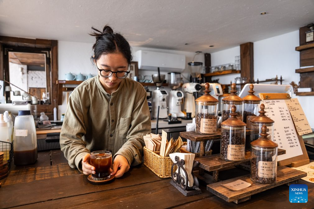 A staff member serves a cup of coffee to a customer at a cafe at a scenic area on the west bank of Fuxian Lake in Yuxi City, southwest China's Yunnan Province, Sept. 14, 2026. In recent years, local authorities have stepped up efforts to protect ecological environment of Fuxian Lake and developed more lakeside activities, combining the natural scenery with local fishing culture to create more consumption experiences. (Xinhua/Hu Chao)