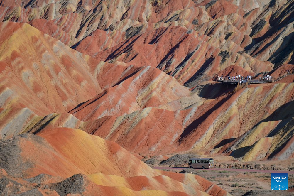 A vehicle drives on a road at the Zhangye Danxia Scenic Area, renowned for its Danxia landforms featuring striking red sandstone formations, in Zhangye, northwest China's Gansu Province, Aug. 4, 2026. The scenic area in Gansu has entered its peak tourism season since August, with the average daily number of visitors surpassing 25,000. (Xinhua/Liu Keying)