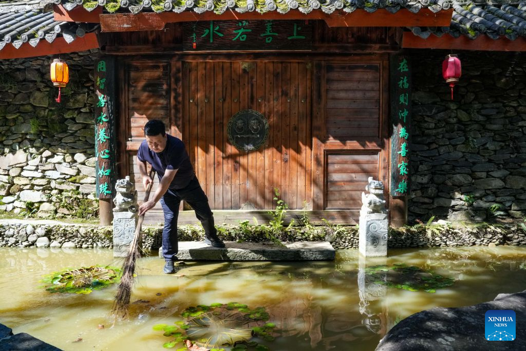 A homestay owner clears fallen leaves at a fish pond in Kangxian County of Longnan City, northwest China's Gansu Province, Aug. 4, 2026. Kangxian, which suffered from heavy rainfall recently, has initiated campaigns to clear up rivers and restore drinking water facilities in the county, striving to bring people's work and daily life back to normal. (Xinhua/Lang Bingbing)