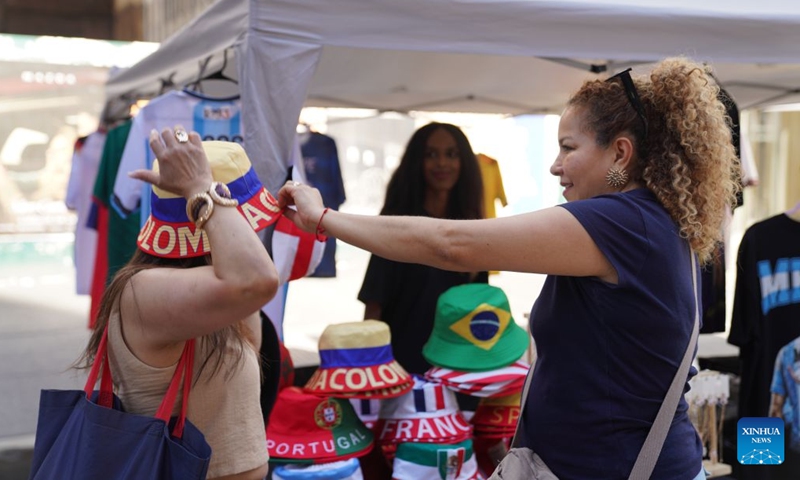 A woman tries on a hat at the Avenue of the Americas Summer Expo at middle town of Manhattan in New York, the United States, on June 21, 2026. (Xinhua/Zhang Fengguo)

