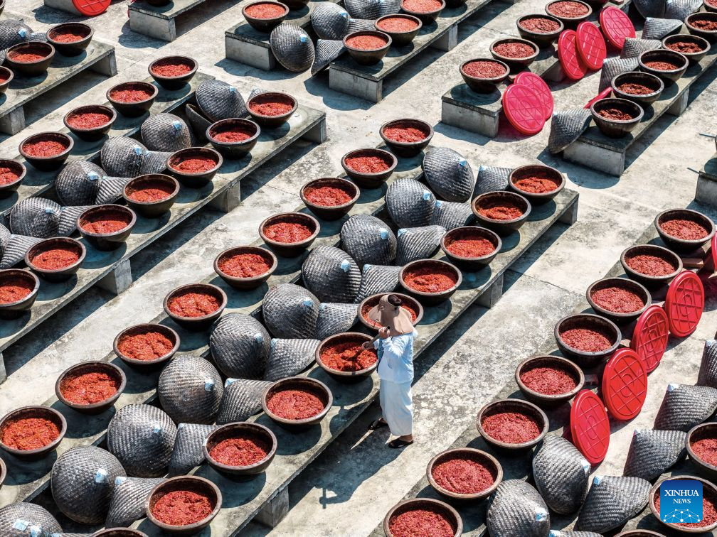 An aerial drone photo taken on Aug. 16, 2026 shows a staff member operating at an airing field for chili sauce in Yongfeng Subdistrict of Shuangfeng County, Loudi City of central China's Hunan Province. As one of China's protected geographical indication products, chili sauce made in Yongfeng Subdistrict boasts a history of several centuries. (Photo by Li Jianxin/Xinhua)