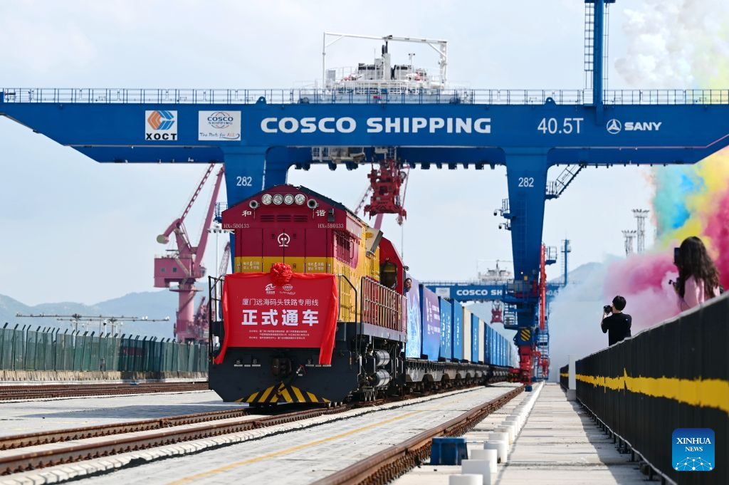 A freight train loaded with containers on a sea-rail intermodal rail line is pictured departing from a quay in Xiamen, southeast China's Fujian Province, July 29, 2026. The sea-rail intermodal rail line is among China's first batch of key projects promoting the integration of transport and logistics. Stretching 1,586 meters, it is designed to handle an annual throughput of 250,000 TEUs of containers and 250,000 tonnes of bulk cargo.
Running perpendicularly to the shoreline and located just 70 meters from the quay apron, the rail line enables cargo to be transferred directly from ships to trains for onward transport. (Xinhua/Lin Shanchuan)