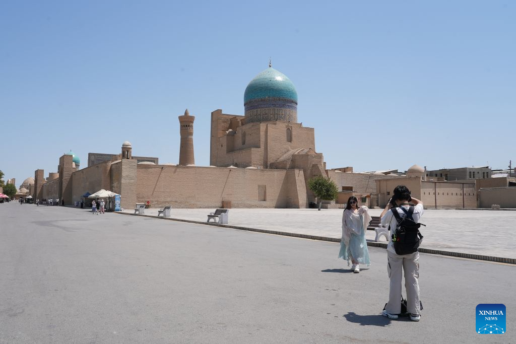 A tourist takes photos in front of historic architecture in Bukhara, Uzbekistan, Aug. 3, 2026. The historic city of Bukhara in southwestern Uzbekistan is currently gripping with severe heat, with daytime highs consecutively exceeding 35 degrees Celsius. (Photo by Zafar Khalilov/Xinhua)