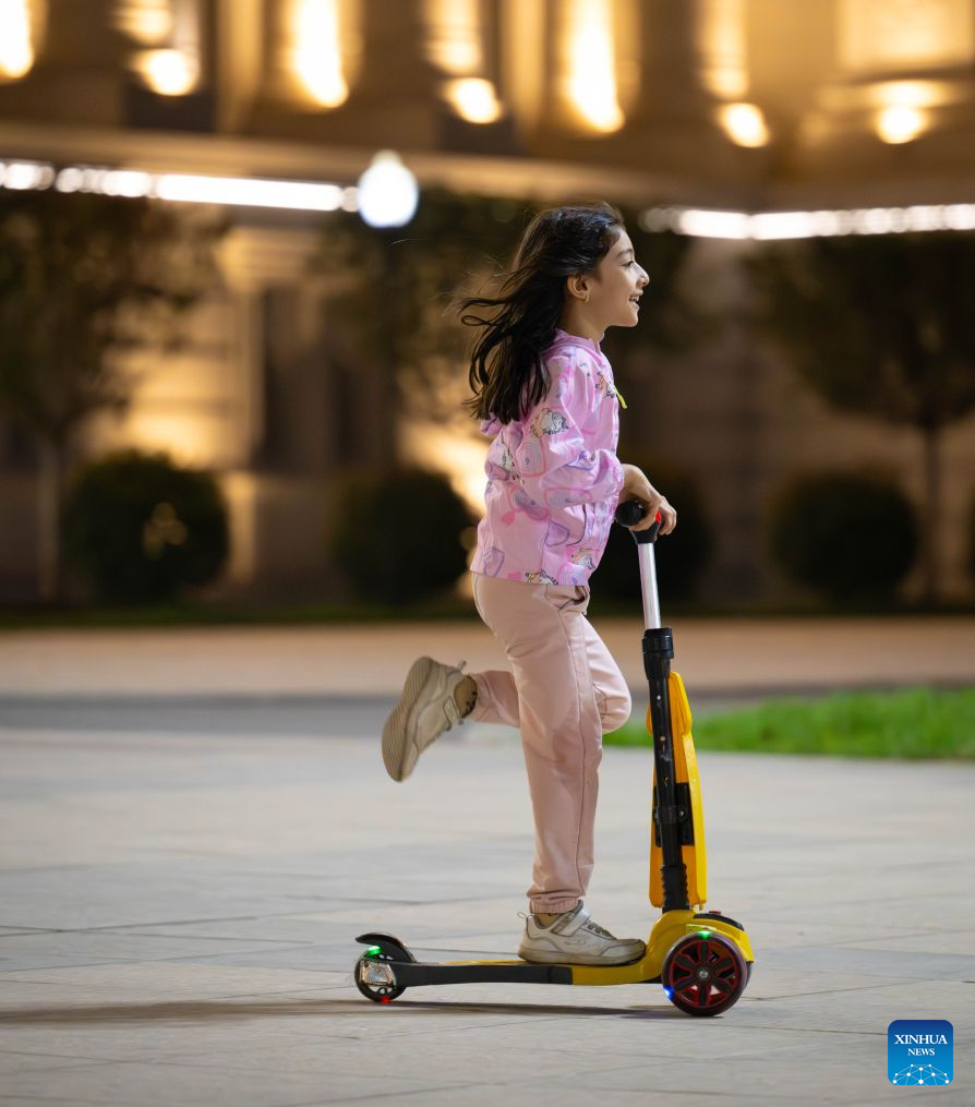 A child rides a scooter in front of the Tajikistan parliament building in Dushanbe, Tajikistan, on Sept. 27, 2026. (Xinhua/Li Renzi)