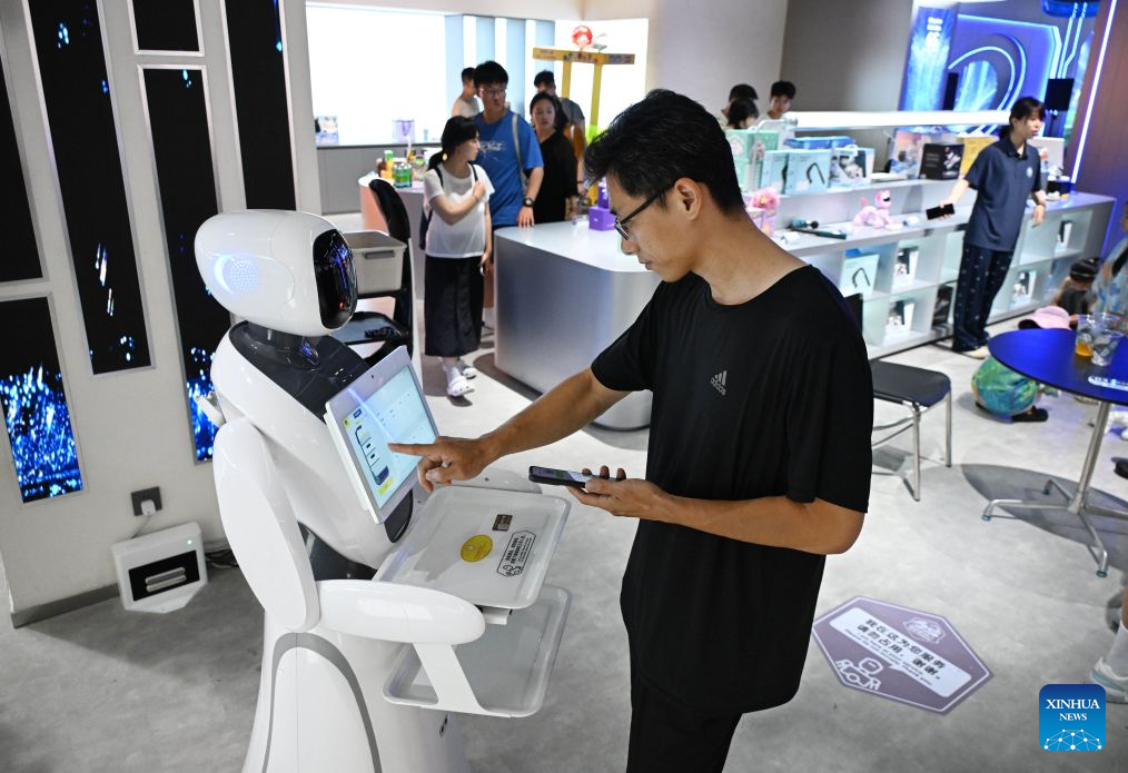 A man interacts with a robot at a robot 6S experience store in Qingdao, east China's Shandong Province on Aug. 11, 2026. Recently, the first robot 6S experience store in Qingdao opened, attracting a large number of consumers to visit and experience. This store integrates six major functions including sale, spare parts, service, survey, lease and personalized customization, helping further introducing robots into people's lives. (Xinhua/Li Ziheng)