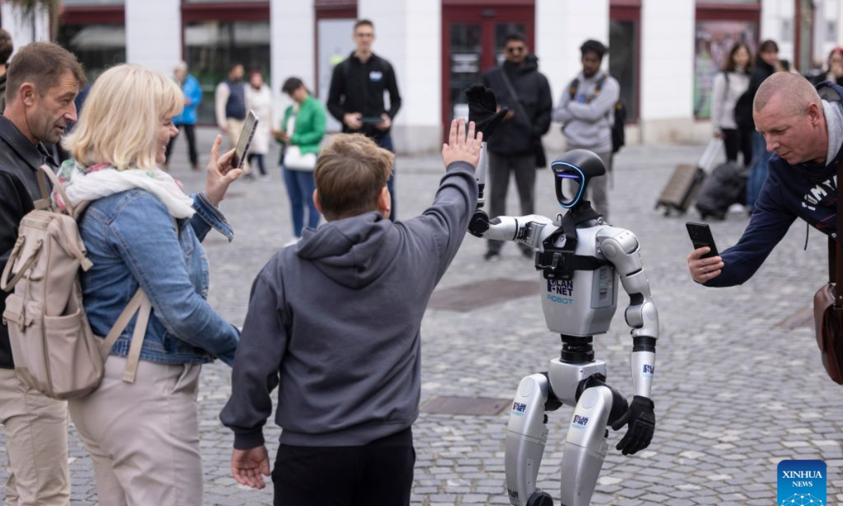 A visitor gives a high-five to the Unitree G1 humanoid robot conductor before the parade of the Ljubljana Wind Orchestra in Ljubljana, Slovenia, Oct. 11, 2026. (Photo by Zeljko Stevanic/Xinhua)
