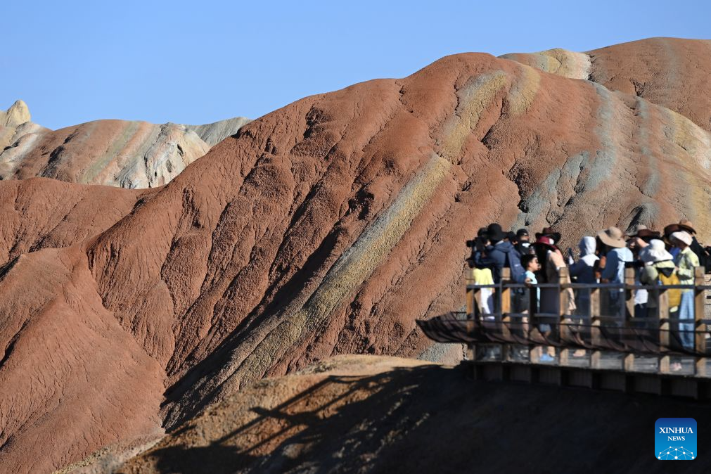 Tourists take photos at the Zhangye Danxia Scenic Area, renowned for its Danxia landforms featuring striking red sandstone formations, in Zhangye, northwest China's Gansu Province, Aug. 4, 2026. The scenic area in Gansu has entered its peak tourism season since August, with the average daily number of visitors surpassing 25,000. (Xinhua/Fan Peishen)