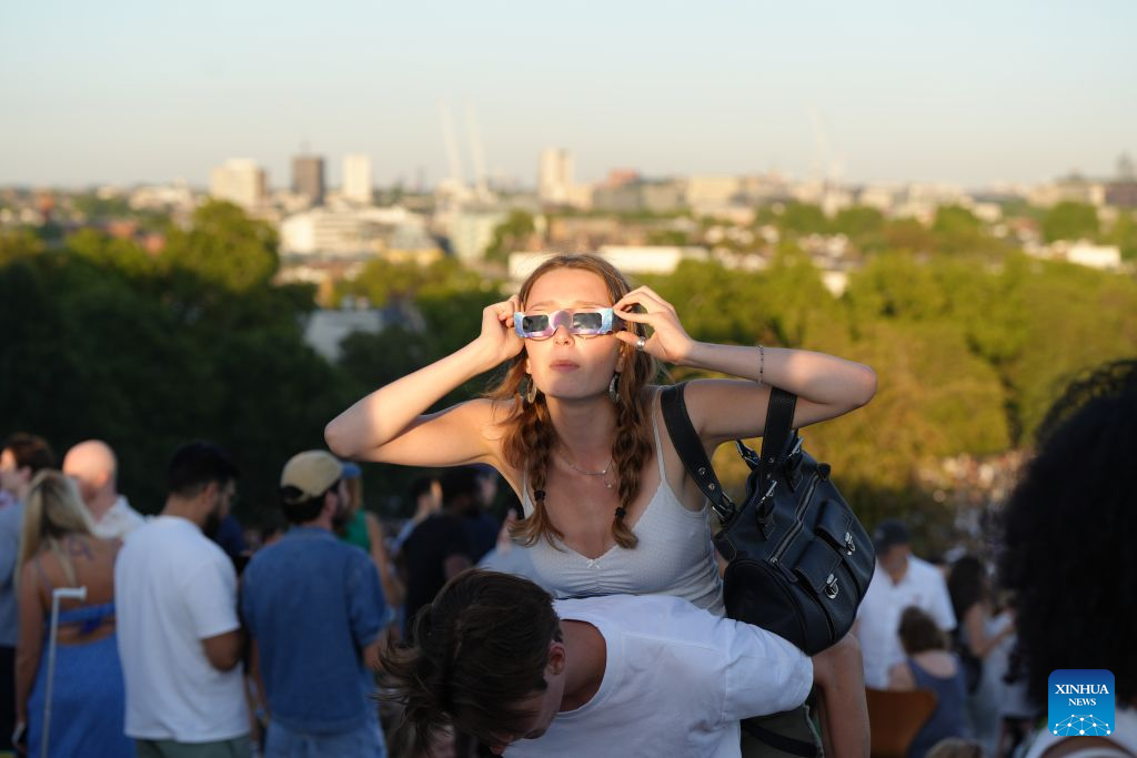 A woman observes the partial solar eclipse on Primrose Hill in London, Britain, Aug. 12, 2026. (Xinhua/Zhang Feng)