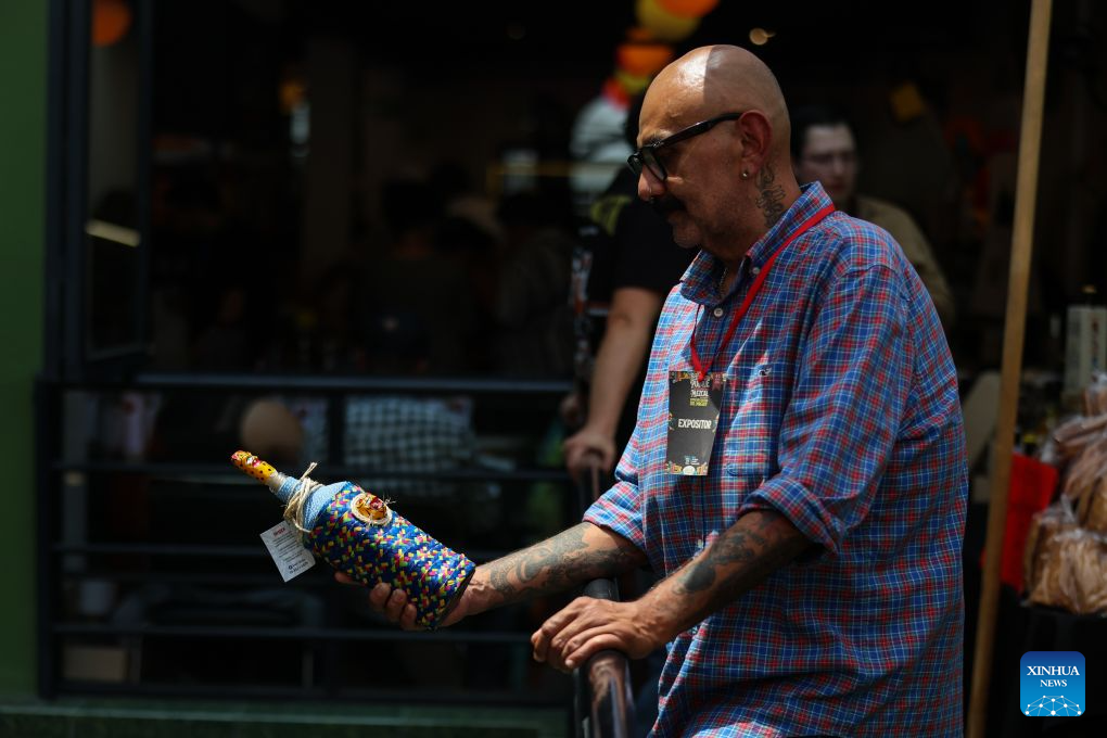 An exhibitor displays a bottle of mezcal, an alcoholic beverage made from the agave plant, decorated with traditional handwoven fabric during the Pulque, Traditional Cuisine and Mezcal Festival in Mexico City, capital of Mexico, Sept. 5, 2026. The event, featuring more than 100 varieties and expressions of agave-based beverages, as well as tastings, food pairings and other activities, was held in Mexico City on Saturday. (Photo by Francisco Canedo/Xinhua)