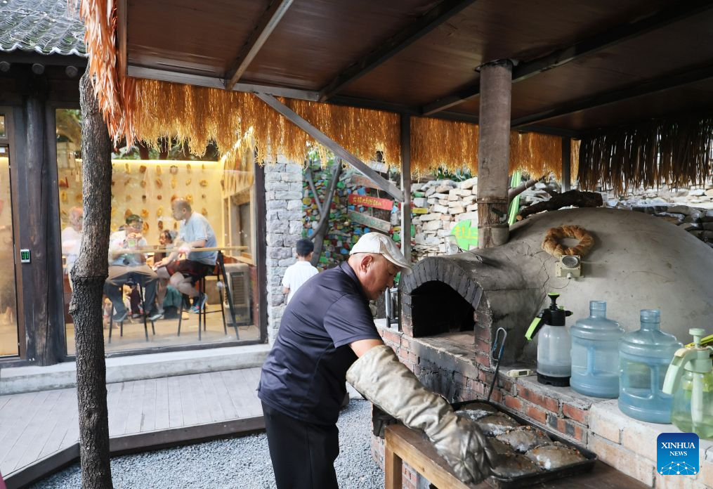 An elderly man bakes bread in Xijingyu Village, Jizhou District of north China's Tianjin Municipality, Aug. 4, 2026. During summer vacation, Xijingyu Village has attracted lots of visitors. Known as the Stone Village, it is famous for its distinctive houses and alleys built of stones. (Xinhua/Li Ran)