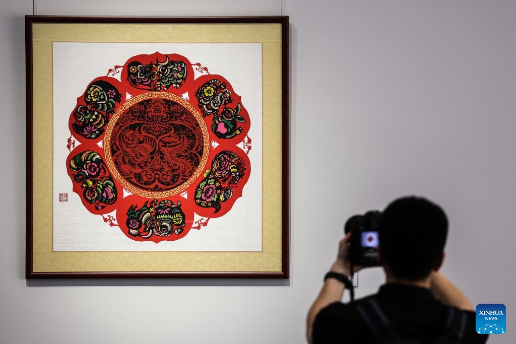 A guest takes photos of an artwork at the Dalian International Conference Center, venue of the 2026 Summer Davos forum, in Dalian, northeast China's Liaoning Province, June 23, 2026. The World Economic Forum's Annual Meeting of the New Champions, also known as the Summer Davos forum, is held in the port city of Dalian from June 23 to 25. An exhibition is open to visitors at the Dalian International Conference Center, featuring more than 1,300 works from 54 forms of intangible cultural heritage. (Photo: Xinhua)