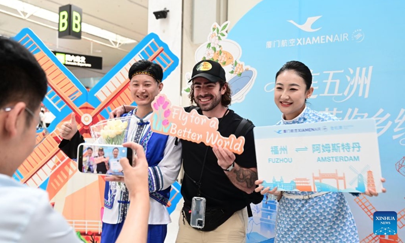 A passenger (C) poses for photos with staff members at a check-in area themed on the first direct flight from Fuzhou to Amsterdam at the Fuzhou Changle International Airport in Fuzhou, southeast China's Fujian Province, June 23, 2026. A direct flight route linking Fuzhou, capital city of southeast China's Fujian Province with Amsterdam, the capital of the Netherlands, was launched on Tuesday. The route is operated by Xiamen Airlines, offering two flights every week. (Photo: Xinhua)