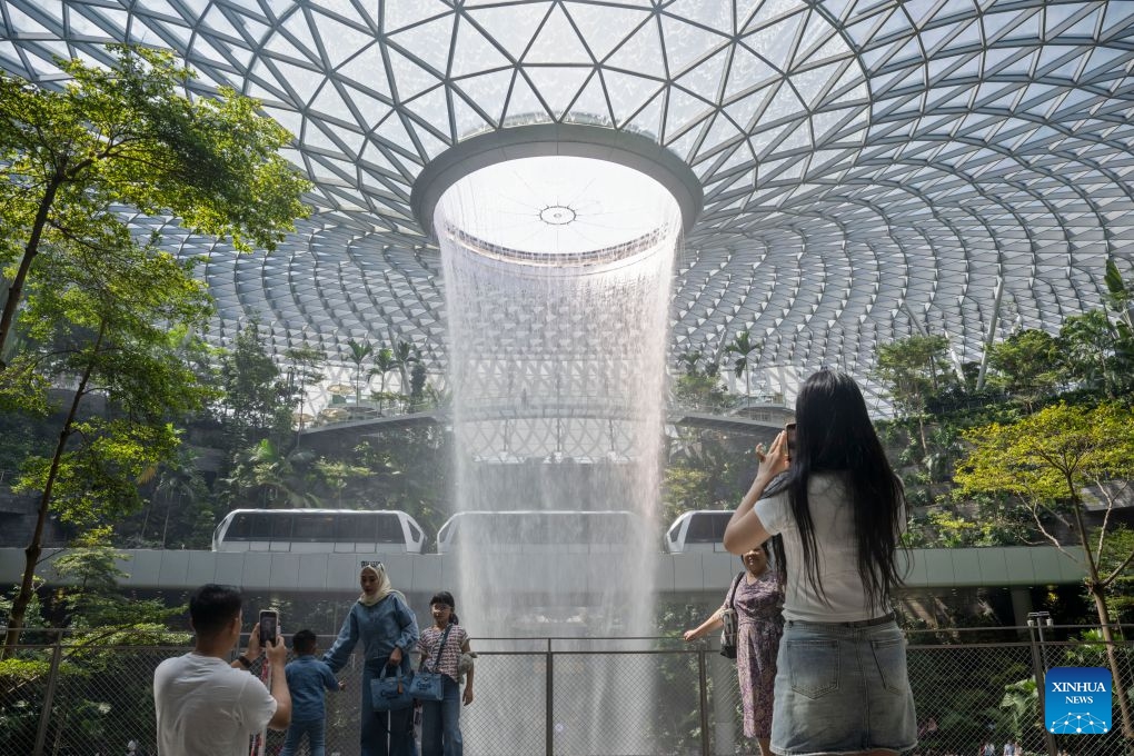 People take photos of the indoor man-made waterfall Rain Vortex at Jewel Changi Airport in Singapore, June 23, 2026. (Photo: Xinhua)