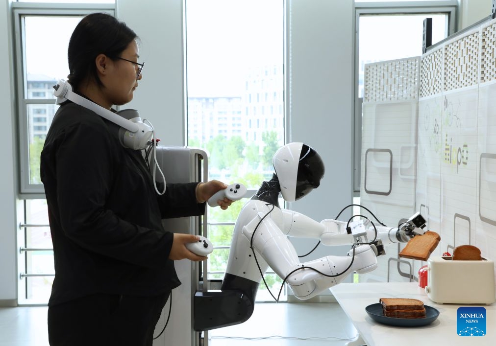 A staff member trains a humanoid robot at a training center for embodied AI in Xiong'an, north China's Hebei Province, June 23, 2026. Xiong'an in Hebei Province has established a training center for embodied AI tailored to various scenarios since December 2025. Equipped with simulated workshops replicating real-world environments, massive amounts of robots' data are generated, making embodied AI increasingly smart and capable of service in all walks of life. (Photo: Xinhua)