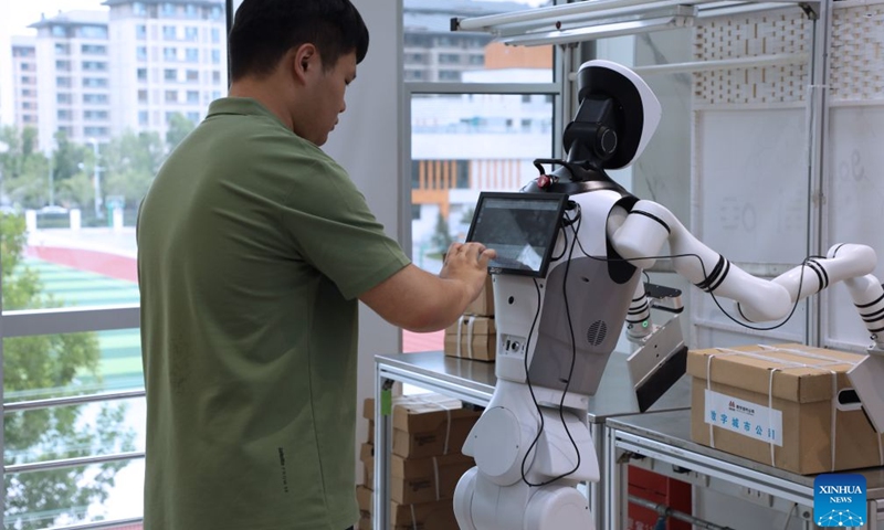 A staff member adjusts a humanoid robot at a training center for embodied AI in Xiong'an, north China's Hebei Province, June 23, 2026. Xiong'an in Hebei Province has established a training center for embodied AI tailored to various scenarios since December 2025. Equipped with simulated workshops replicating real-world environments, massive amounts of robots' data are generated, making embodied AI increasingly smart and capable of service in all walks of life. (Photo: Xinhua)