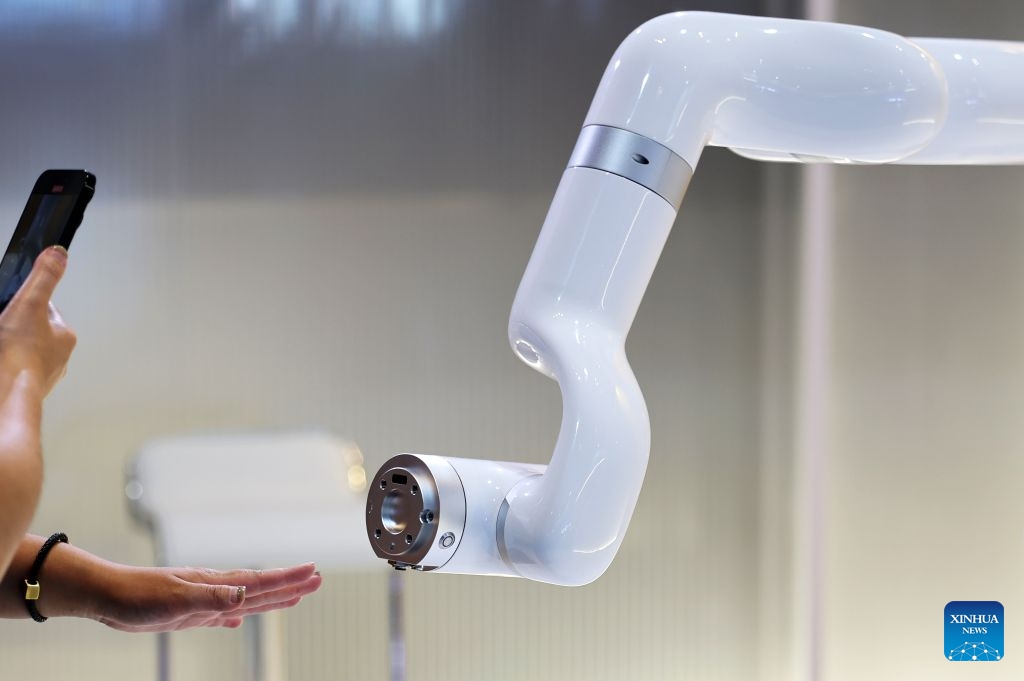 A participant interacts with a robotic arm during the 17th Annual Meeting of the New Champions, also known as the Summer Davos, at the Dalian International Conference Center in Dalian, northeast China's Liaoning Province, June 24, 2026. Featuring the theme Innovating at Scale, the event is held from June 23 to 25. Over 30 subjects related to artificial intelligence and robotics are among the hot topics at this year's forum. (Photo: Xinhua)
