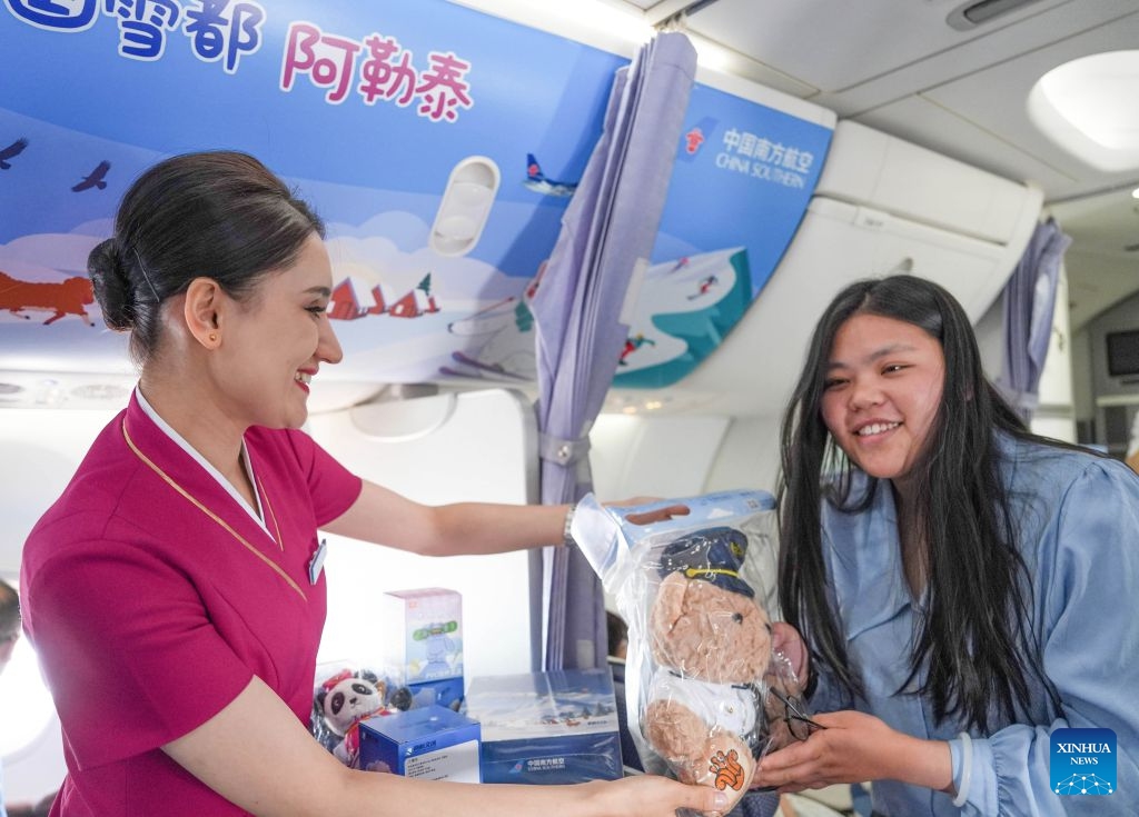 A flight attendant presents a souvenir to a passenger aboard a painted plane from Altay in northwest China's Xinjiang Uygur Autonomous Region to Beijing, June 24, 2026. China Southern Airlines held a launching ceremony for a painted plane on Wednesday, following which the plane will operate the flight from Altay to Beijing Daxing International Airport. (Photo: Xinhua)
