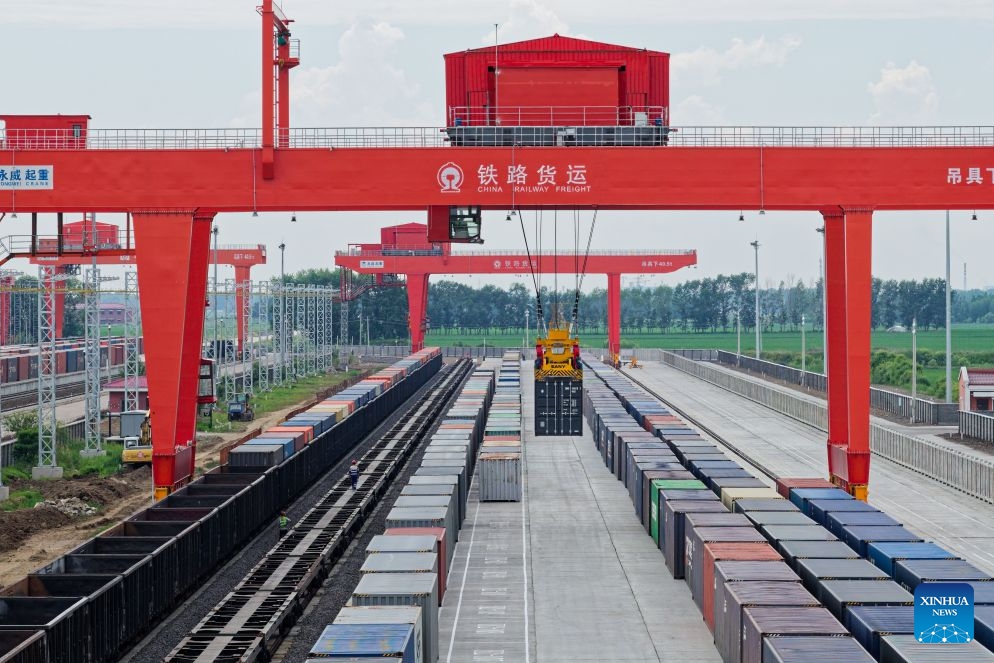 A drone photo taken on June 24, 2026 shows a crane lifting a container at a yard of transshipment operation of the Tongjiang North Railway Station in Tongjiang, northeast China's Heilongjiang Province. By June 23, Tongjiang railway port has handled 128 China-Europe freight train trips with 115,724 tonnes of goods, increasing by over 100 percent year on year. (Photo: Xinhua)