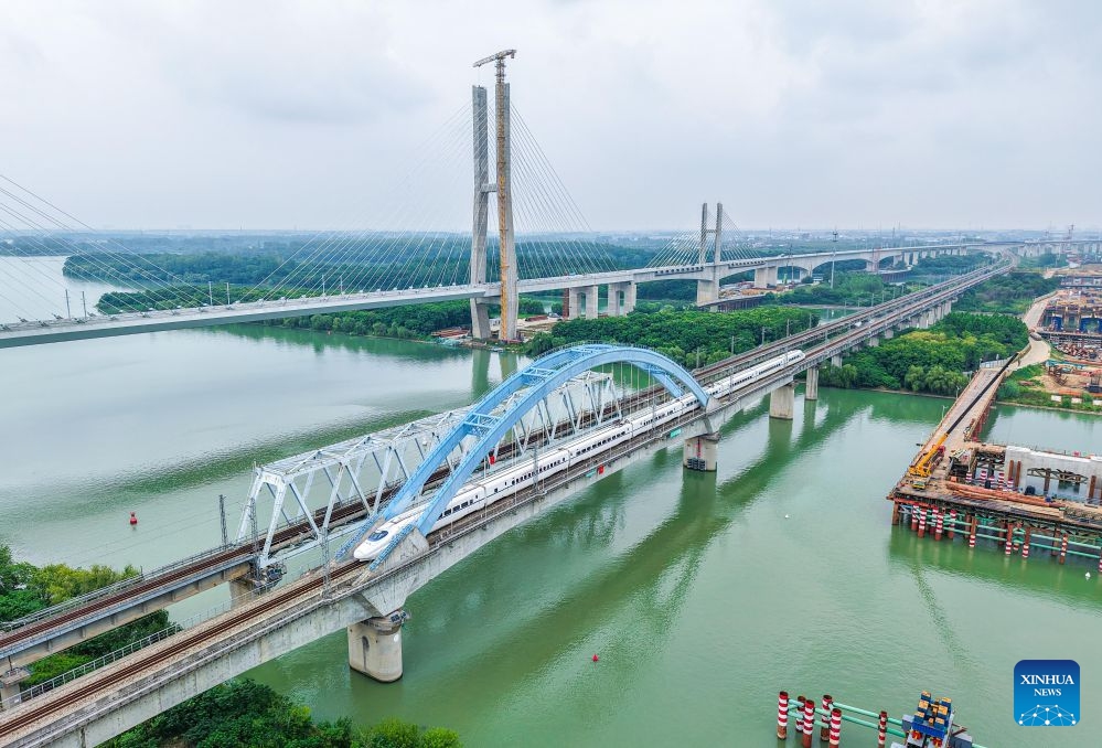 A drone photo taken on June 30, 2026 shows a high-speed train passing a bridge in Yangzhou, east China's Jiangsu Province. Starting from 00:00 on July 1, China's railway diagram will be adjusted by adding 106 passenger train services and 111 freight train service to the current schedule. After the adjustment, a total of 12,174 passenger trains will be scheduled nationwide, while 23,975 freight trains will be operated. (Photo by Ren Fei/Xinhua)