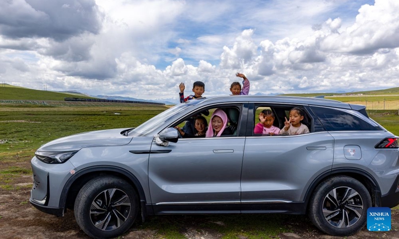 Tatso sits in her car with children, as a train is seen in the background, in Damxung County of Lhasa, southwest China's Xizang Autonomous Region, June 21, 2026. Twenty-one years ago, as the construction of the Qinghai-Xizang Railway was in full swing, Xinhua photojournalist Chogo took a vivid photo at the construction site in Damxung County on March 30, 2005. In the picture, two girls were sitting beside a rail with bright smiles on their faces. (Photo: Xinhua)