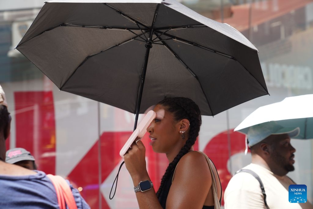 A woman cools off with an umbrella and a mini fan during a heat wave in New York, the United States, on July 2, 2026. (Xinhua/Zhang Fengguo)