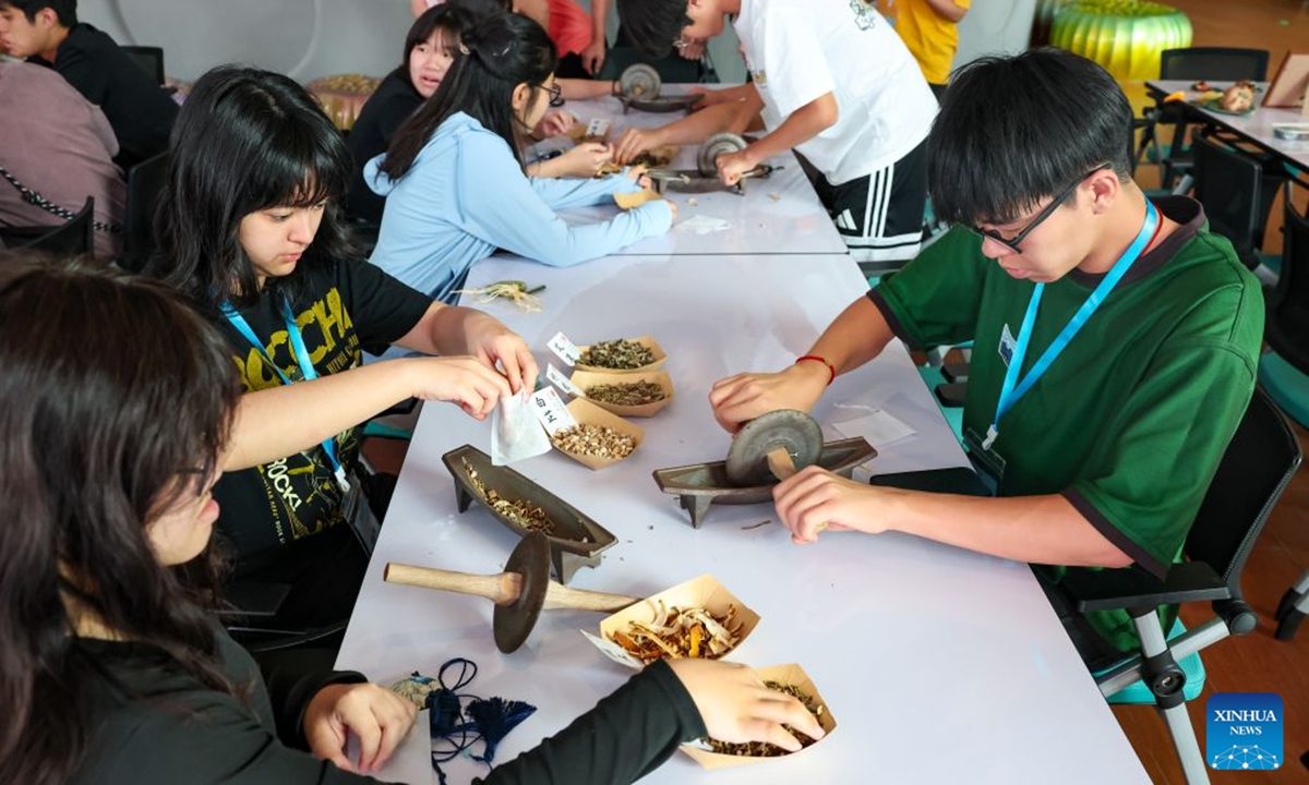 Students try grinding traditional Chinese medicinal herbs at an experience center of Guangdong-Macao Traditional Chinese Medicine Technology Industrial Park in Hengqin, Zhuhai City, south China's Guangdong Province, July 2, 2026. Hengqin, located in Zhuhai, Guangdong Province, is separated from Macao by a narrow stretch of water. The Guangdong-Macao In-Depth Cooperation Zone in Hengqin was established in 2021 to facilitate Macao's better integration into the overall national development. (Xinhua/Zhang Yudong)