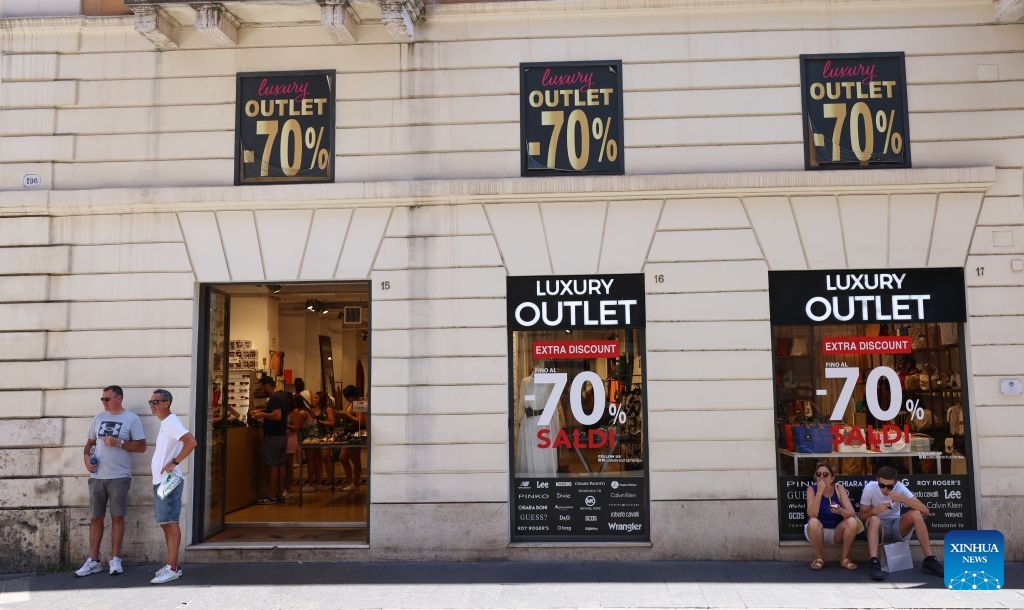 People rest near a shop with sale advertisements on its windows in Rome, Italy, July 4, 2026. Most regions across Italy have kicked off their summer sales. (Xinhua/Wang Kaiyan)