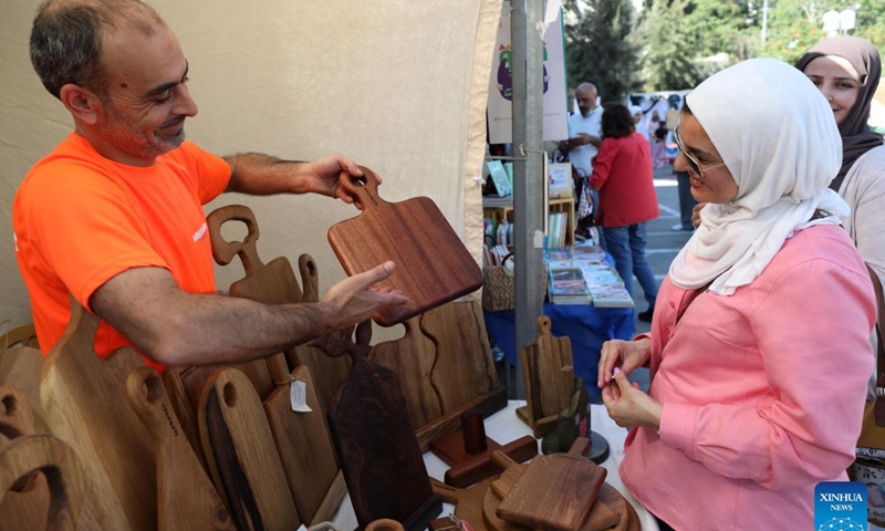 A vendor introduces a product at the Harjeh Market in the West Bank city of Ramallah, July 3, 2026. The market is a vibrant cultural event that brings together a diverse selection of traditional handicrafts, handmade products, and local foods, offering visitors an opportunity to experience the richness and diversity of Palestinian heritage. It is held every Friday in Ramallah's Old Town from late June through early August. (Photo by Ayman Nobani/Xinhua)