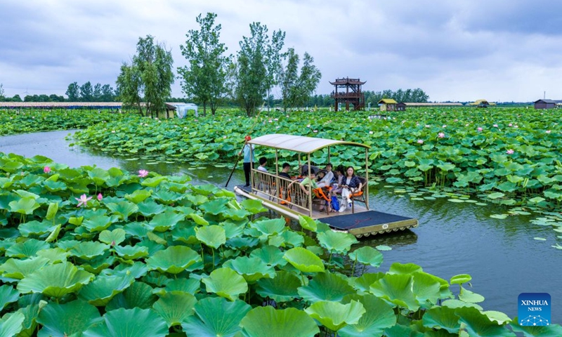 A drone photo shows children taking a raft to enjoy lotus flowers with their parents at a scenic spot in Xinghua City, east China's Jiangsu Province, July 5, 2026. (Photo by Zhou Shegen/Xinhua)