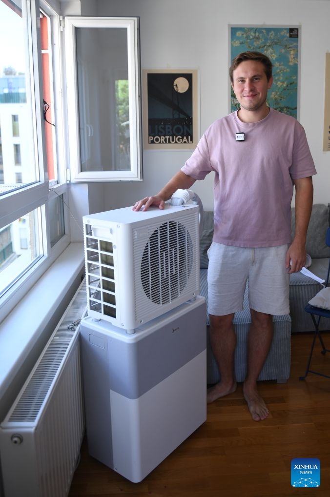 Denis Yurchak poses for photos with a Midea Portasplit mobile split air conditioner at his apartment in Vienna, Austria, July 4, 2026. For Austrian resident Denis Yurchak, the search for an air conditioner to survive this year's scorching summer felt like embarking on an adventure.

