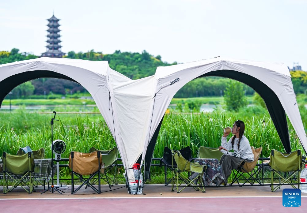 A visitor enjoys herself in a camp on the bank of Hutuo river in Shijiazhuang, north China's Hebei Province, July 5, 2026. Shijiazhuang has developed a camping-based tourism brand to enrich short-getaway options for tourists, boost consumption and promote rural revitalization. (Photo: Xinhua)