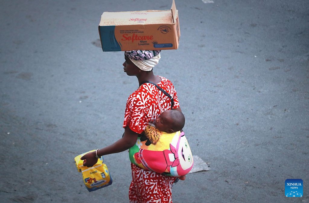 A woman carries her child on her back while selling goods on a street in Abidjan, Cote d'Ivoire, on July 9, 2026. (Photo: Xinhua)