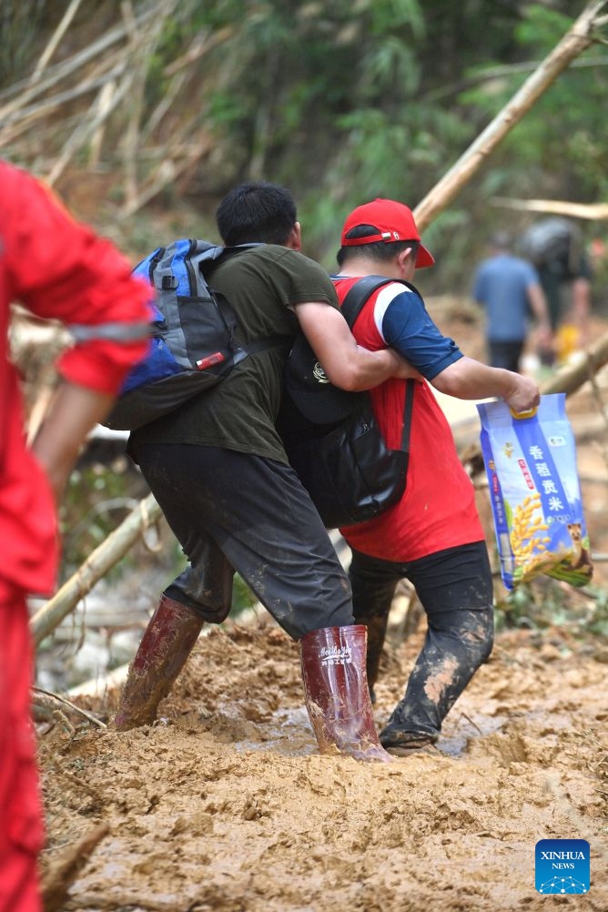 Li Henghao (L) helps members of a supplies transport team cross a collapsed section of a road in Zhenlong Township, Hengzhou City, Nanning, south China's Guangxi Zhuang Autonomous Region, July 10, 2026.