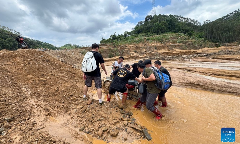 Li Henghao (1st R, front) helps a motorcyclist push a motorcycle out of muddy water in Zhenlong Township, Hengzhou City, Nanning, south China's Guangxi Zhuang Autonomous Region, July 10, 2026.